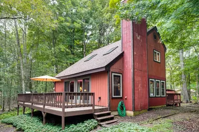 a red house with a deck in the woods at Pocono Lake Retreat Ski and Explore at Pine Loch! in Pocono Lake