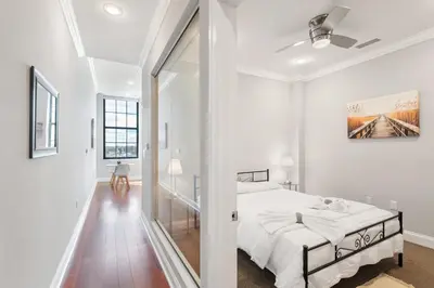 a white bedroom with a bed and a hallway at Glam Flat with View, Pool, Deck in Philadelphia