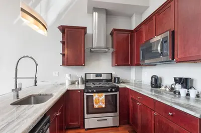 a kitchen with wooden cabinets and a stove top oven at Glam Flat with View, Pool, Deck in Philadelphia