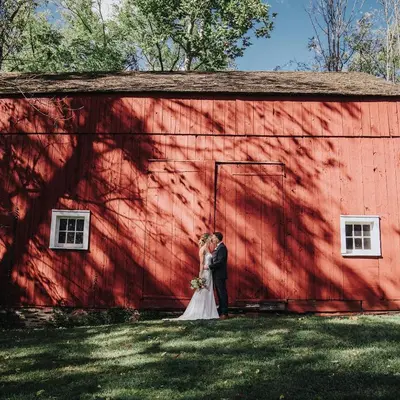 a bride and groom standing in front of a red barn at Inn at Glencairn in Princeton