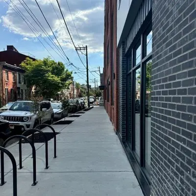 a sidewalk with benches next to a brick building at Landing at Hagert and York 1 Bedroom in East Kensington in Philadelphia