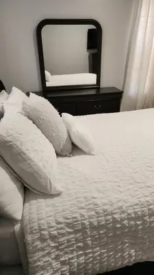 a bed with white pillows and a large mirror at Comfortable Apartment in Irvington