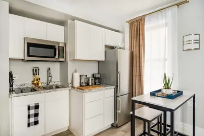 a kitchen with white cabinets and a table and a refrigerator at 73-308 New 1BR 1Bth UWS Doorman Gym in New York