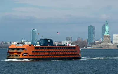 an orange boat on the water with the statue of liberty at New York City Apartment Near Free Ferry Boat! in Stapleton