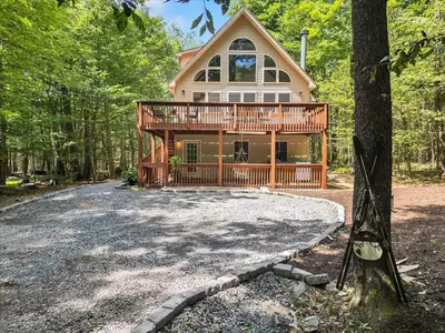a house with a wrap around deck in the woods at Chalet Lake, Movie Theater, Hot Tub, Arcade in Gouldsboro