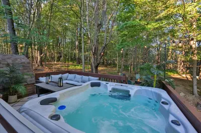 a hot tub on a patio in the woods at Winter Hideaway - Sled Hill, Hot Tub, Fireplace, Game Room in Gouldsboro