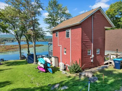a red house with a boat in front of it at Lakefront, Hot Tub, Dock, Kayaks, Amazing Views in Lake Ariel