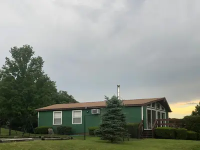 a green house with a tree in front of it at Fenced Yard Chalets from Good Dog Vacations at Big Valley Resort in Sciota