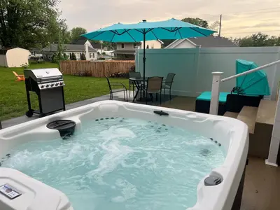 a hot tub in a backyard with a grill and an umbrella at Perfect Family Getaway! Steps from Attractions in Hummelstown