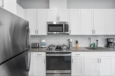 a kitchen with white cabinets and a stainless steel refrigerator at Jersey City's Best Enjoy Our Deluxe 1 Bedroom Condo Only 25 Minutes to NYC in Jersey City