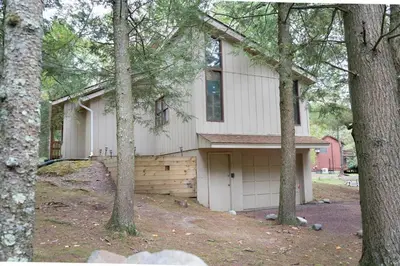 a white house with a garage in the woods at Racc00ns Retreat in Lake Harmony