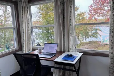 a desk with a laptop computer on it in front of a window at 5-Bedroom Lakefront, private beach wifi AC boat & in Tobyhanna