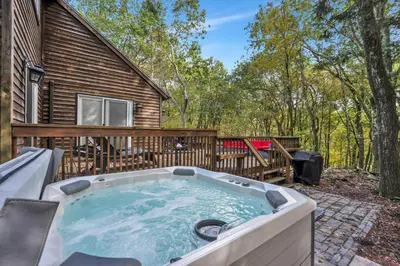 a hot tub on a patio next to a house at Nature's Paradise with Hot Tub and Fire Pit in Lake Harmony