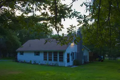 a small white house in a field with trees at Cozy Pocono Home with a Hot Tub, Fire pit, Karaoke, Games and more! in Albrightsville