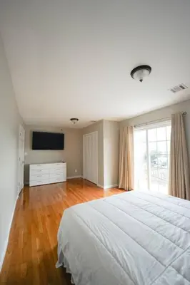 a white bedroom with a large bed and a television at Newark Liberty Brick House - Private Bedroom 1 in Newark