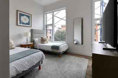 a bedroom with two beds and a tv and a window at Prime Hoboken Lofts in Hoboken