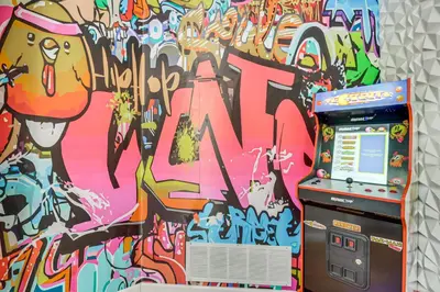 an arcade machine in front of a wall with graffiti at Chic Pocono Hideaway with Private Indoor Sauna in Long Pond