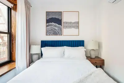 a bedroom with a bed with a blue headboard and two lamps at 48-3FE 2BR Prime Midtown West in New York
