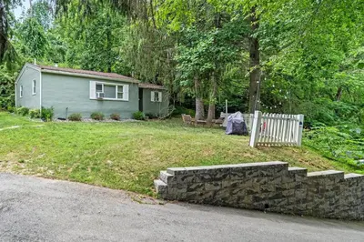 a small house with a stone wall in front of a yard at Quiet Cottage In The Woods, with Hot Tub! in Glenmoore