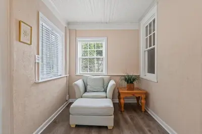 a room with a chair and a table and two windows at Stay At Our Tasteful, Private, & Elegant Abode in Devon