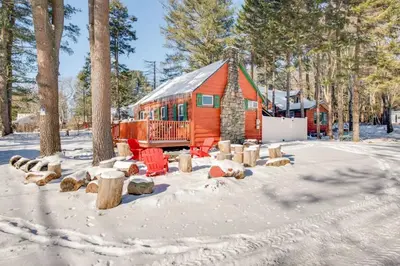 a cabin in the snow with red chairs and trees at The Rustic Cabin in Blakeslee