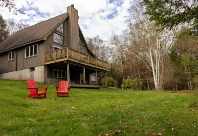 two red chairs sitting in the grass in front of a house at Private Chalet with Fire Pit Deck and Large Yard in Roscoe