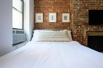 a white bed in a room with a brick wall at 24-10 Studio in Prime Gramercy WD in Unit in New York