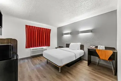a bedroom with a bed and a desk with a red curtain at Studio 6 King of Prussia PA Philadelphia in King of Prussia