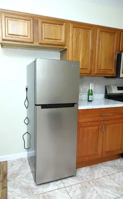 a stainless steel refrigerator in a kitchen with wooden cabinets at Spacious 3 Bedroom, 15 Min to EWR Airport and Parks in Newark