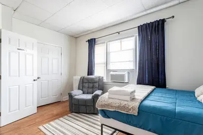 a bedroom with a bed and a chair and a window at Deluxe 4BR 2BA Apartment Near NYC and Airport in Bayonne