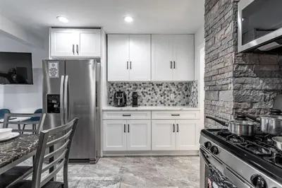 a kitchen with white cabinets and a stainless steel refrigerator at The Modern Retreat 4BR 2BA Near NYC and Airport in Bayonne