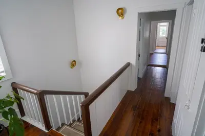 a hallway with white walls and wooden floors and stairs at Stylish Apt Walk to Shops, Dining, and Bucknell in Lewisburg