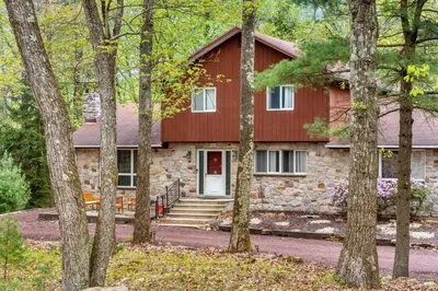 a red house with a red door in the woods at Pocono Retreat Hot Tub MovieRoom GameRoom etc in Lake Harmony