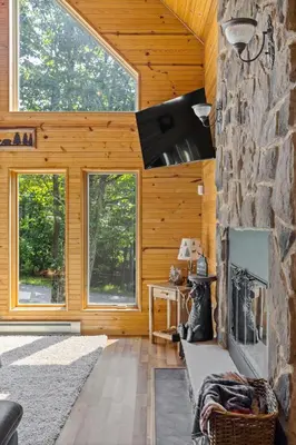 a living room with a stone fireplace and windows at Rustic Retreat - Fire-pit Hot-Tub and more in Albrightsville