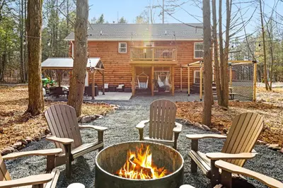 a fire pit with chairs and a log cabin at Cozy Cinema Cabin - Hot Tub and More in Blakeslee