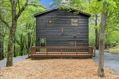 a black house with a porch in the woods at Cabin in the Skye - 5 BDs Lake Harmony in Lake Harmony