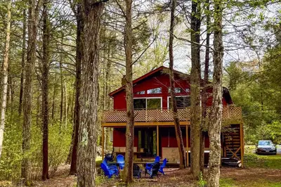 a red cabin with blue chairs in the woods at Hot Tub, Dock, Pool Table! Lakefront Poconos Haven in White Haven