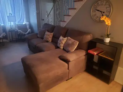 a living room with a brown couch and stairs at Orchard Room by the Airport - Shared Space in Darby