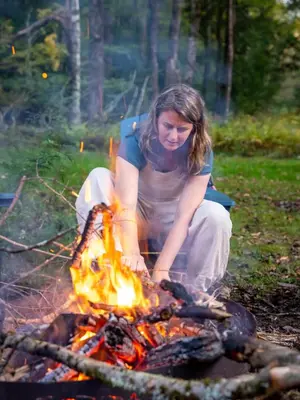 a woman sitting in front of a fire at Waterfront Secluded Log Cabin in Beach Lake