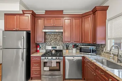 a kitchen with wooden cabinets and stainless steel appliances at HUGE Cozy Jersey City Oasis with Double Balcony - 20 mins to NYC in Jersey City