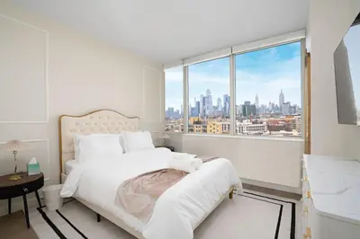 a white bedroom with a view of the city at Midtown View - Minutes to City in Hoboken