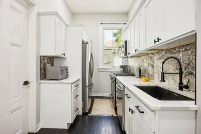 a white kitchen with white cabinets and a sink at Chic & Modern - 30 Mins to NYC in Jersey City