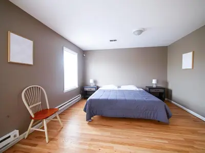 a bedroom with a bed and a chair and two windows at Deluxe 2-Bedroom Apt minutes from NYC in Jersey City