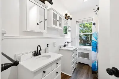 a white bathroom with two sinks and a window at Main Line Manor 3BR with King Beds & Patio & Backyard in Bryn Mawr