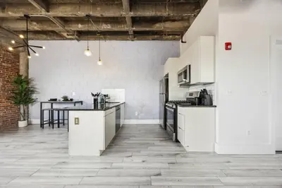 an open kitchen with white cabinets and a brick wall at Lofts at Kearny - Rustic Chic 1-3BR Lofts with Quick NYC Access & On-Site Gym in Kearny