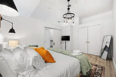 a white bedroom with a bed with orange pillows at Lofts at Kearny - Rustic Chic 1-3BR Lofts with Quick NYC Access & On-Site Gym in Kearny