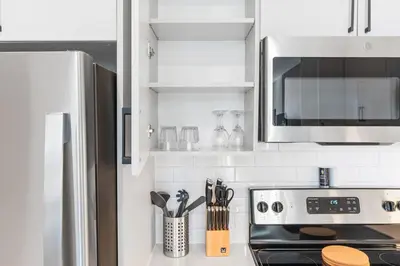 a white kitchen with a stove and a microwave at 5 mins to Fillmore! Queen Bed, Rooftop, NorthernLibs! in Philadelphia