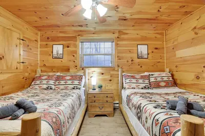 two beds in a log cabin bedroom with wooden walls at Cozy Freeland Retreat- Firepit Pool Table Hot Tub in White Haven