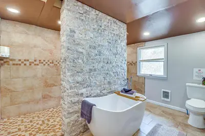 a bathroom with a white tub and a stone wall at Fire Pit and Game Room Spacious Poconos Retreat! in Long Pond