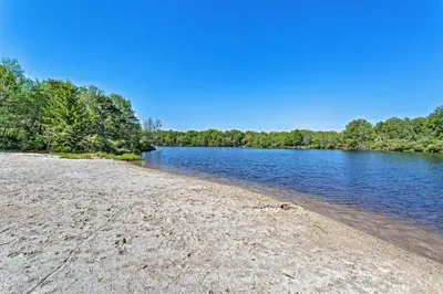 a sandy beach next to a river with trees at Fire Pit and Game Room Spacious Poconos Retreat! in Long Pond